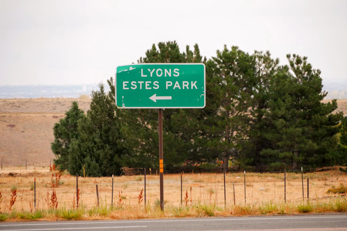 ป้ายบอกทางสีเขียวเก่าซีดเขียนว่า Lyons Estes Park ริมถนนในโคโลราโด