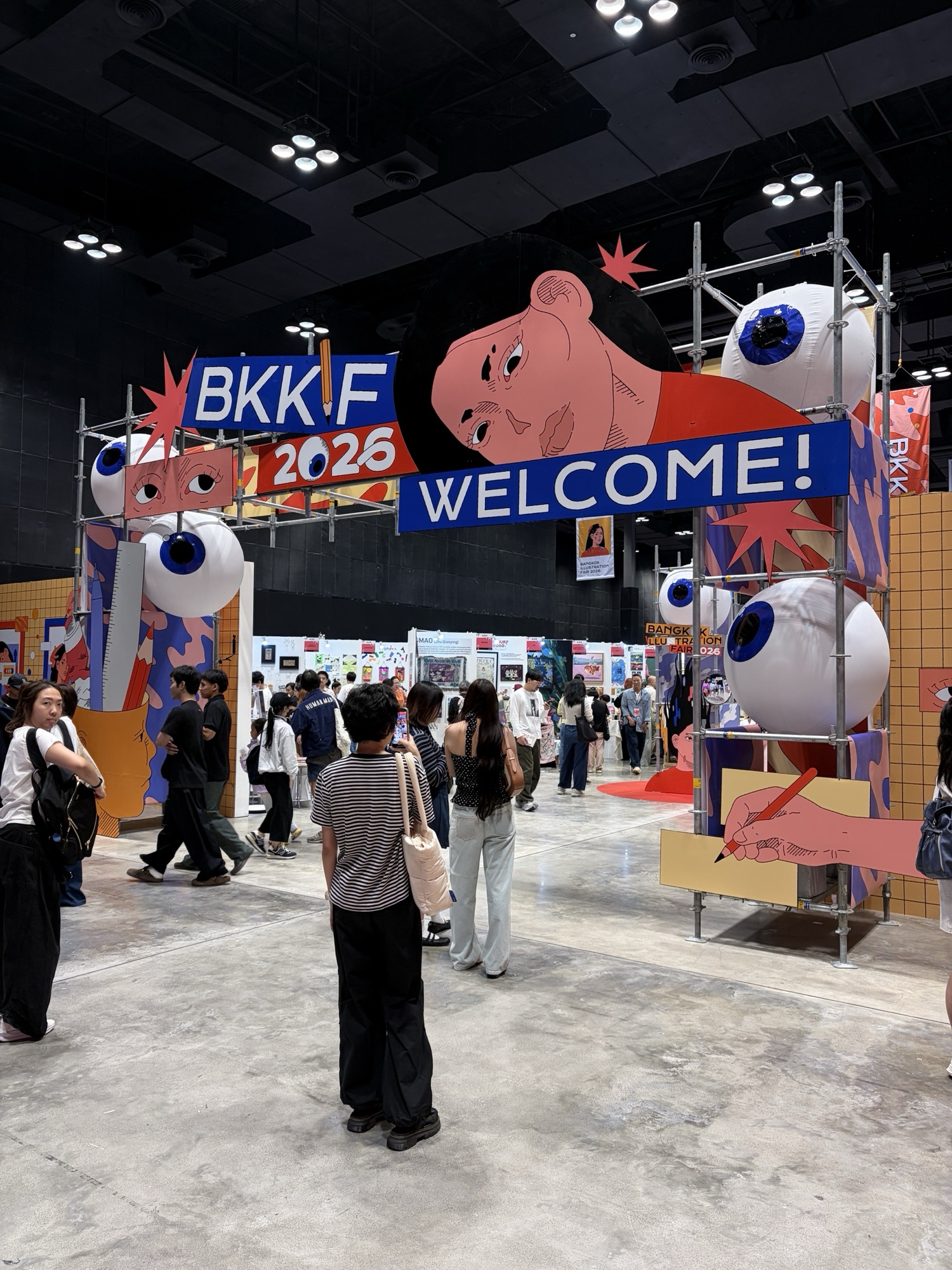 ซุ้มทางเข้า BKKIF 2026 บนนั่งร้านเหล็ก มีหน้าผู้หญิงสีชมพู ลูกตาเป่าลม และป้าย WELCOME