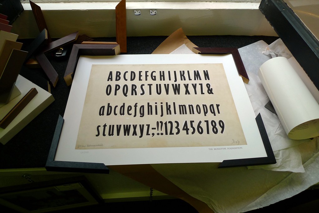 ภาพพิมพ์แบบร่างตัวอักษร Gill Sans แบบตัวหนาบีบแคบ วางอยู่บนโต๊ะพร้อมกรอบรูปเปล่า