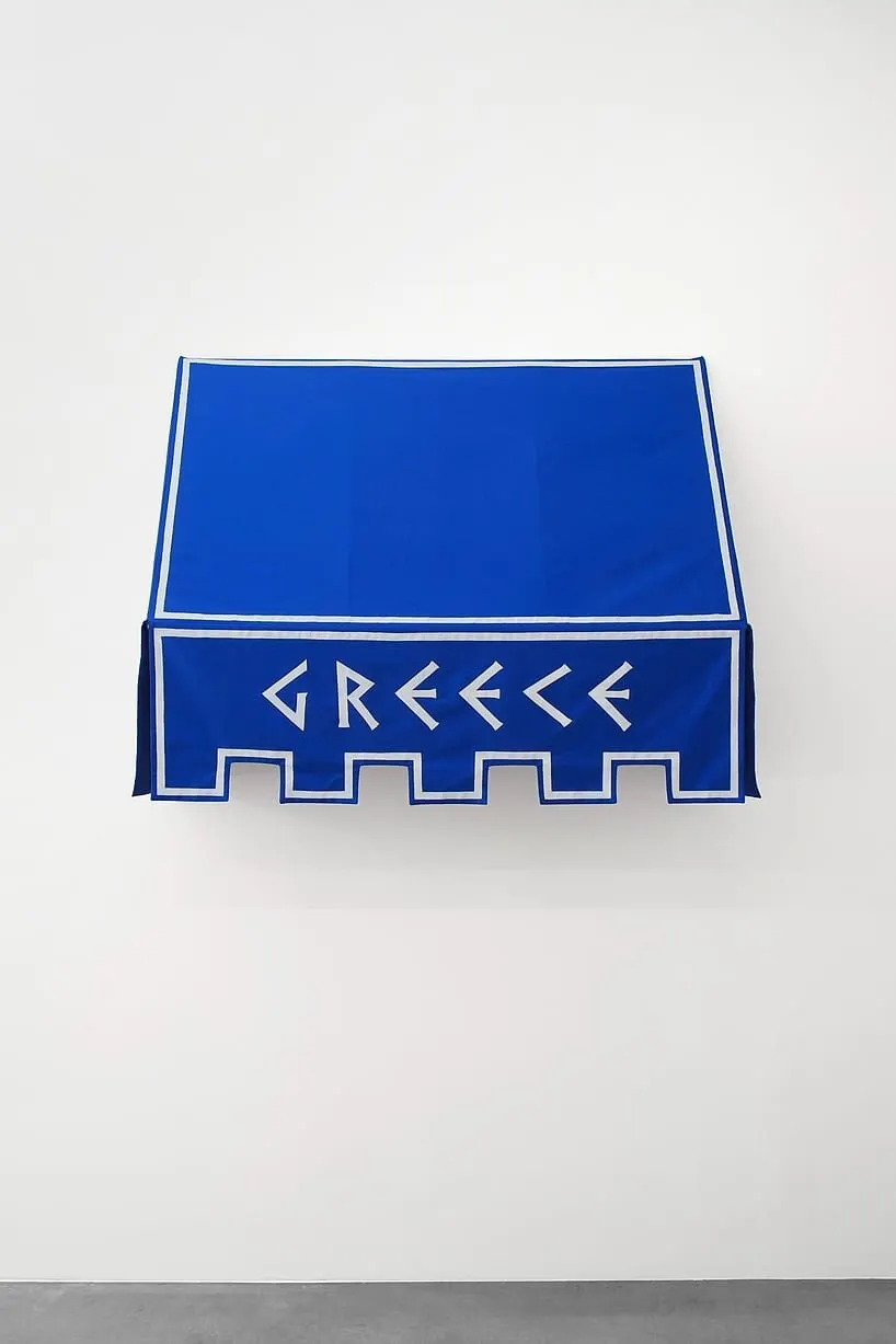 ผ้าใบกันสาดสีน้ำเงินเข้ม คำว่า GREECE ตัวอักษรหักเหลี่ยม ขอบล่างตัดเป็นฟันปราสาท