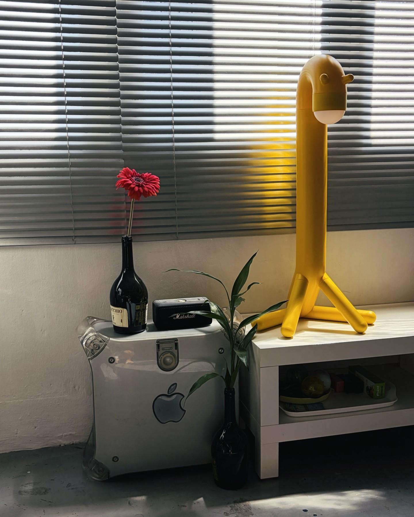 โคมไฟรูปยีราฟสีเหลืองข้างเคสคอม Power Mac G4 ที่มีขวดใส่ดอกเยอบีร่า