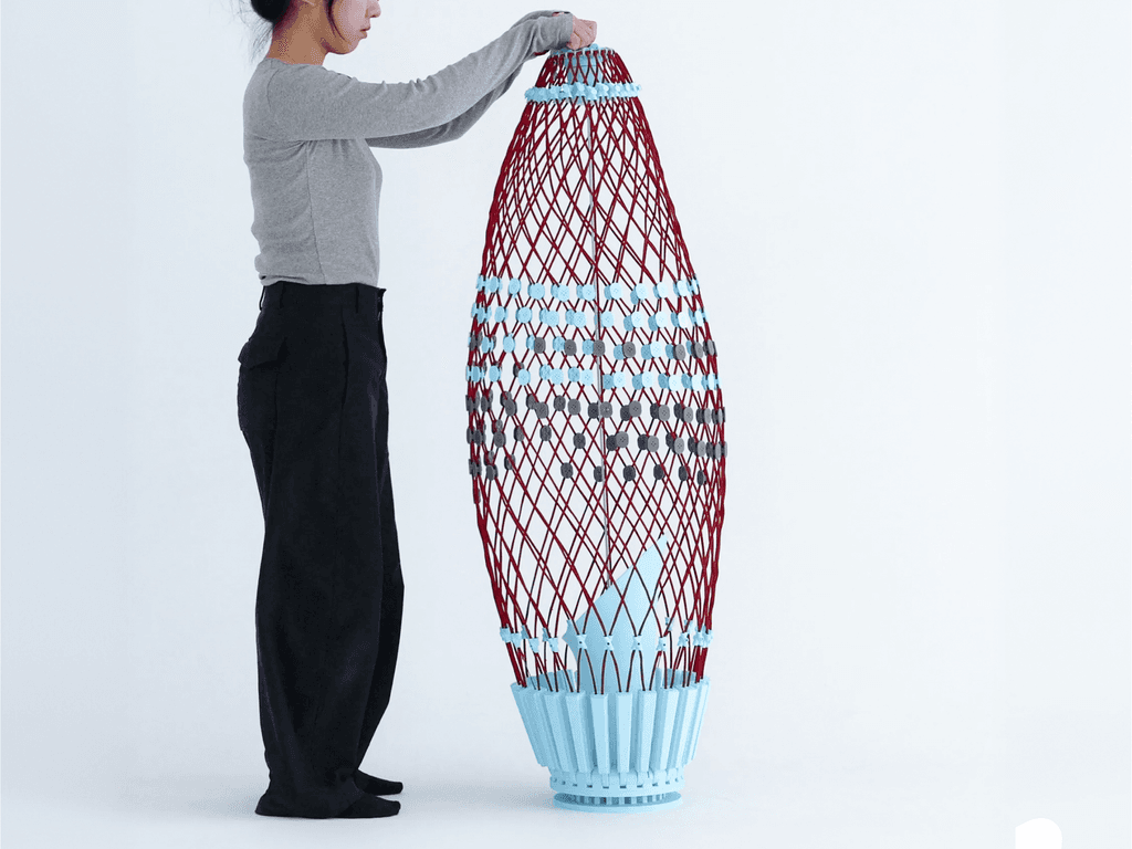 Re-flat Pack Sofa ในสภาพหุบตัว เป็นเสาสูงเรียวสีแดงและฟ้า มีคนยืนจับปลายบนไว้