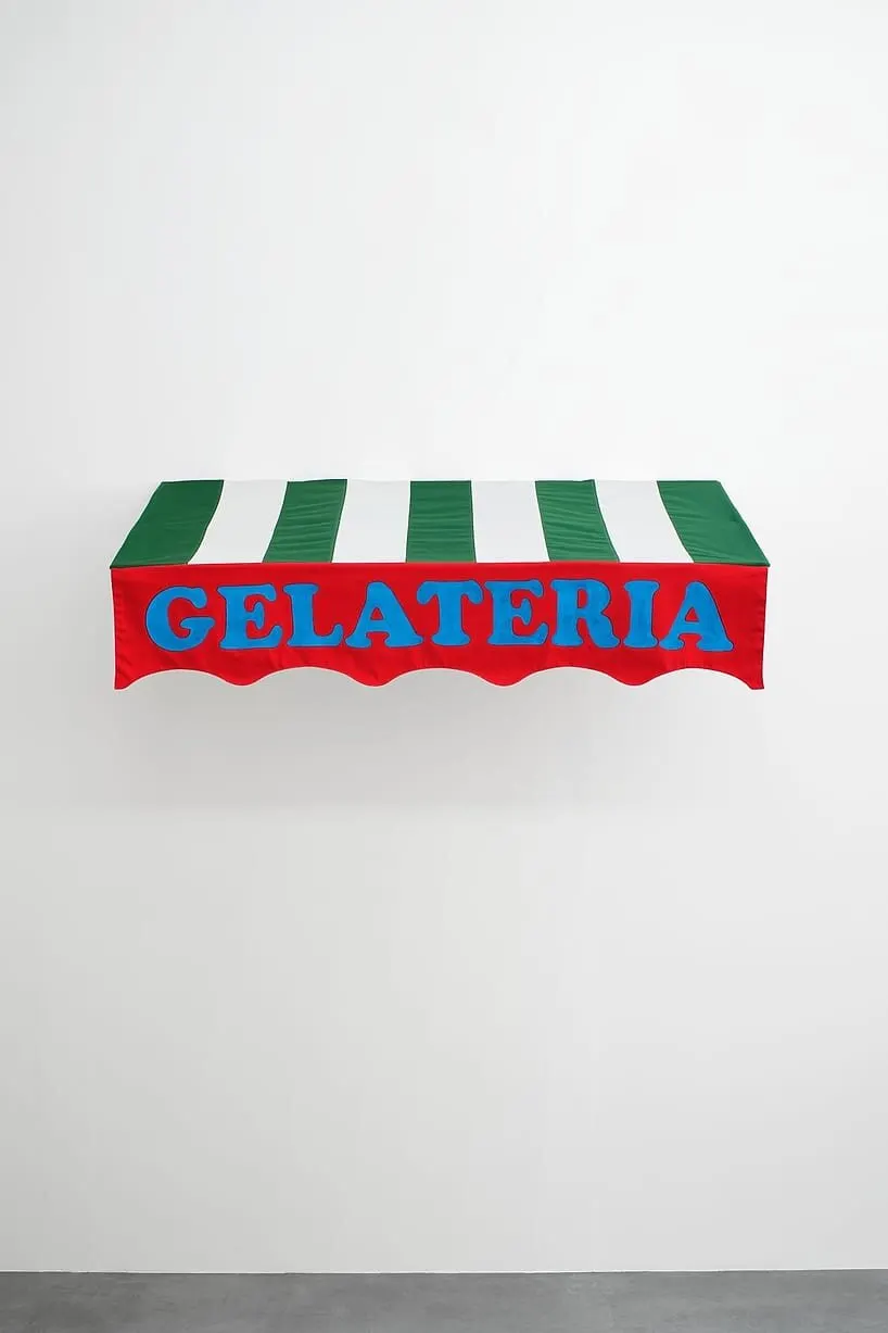 ผ้าใบกันสาดหน้าร้านลายทางเขียวขาว ขอบล่างสีแดงหยักคลื่น มีคำว่า GELATERIA ตัวอักษรสีฟ้า