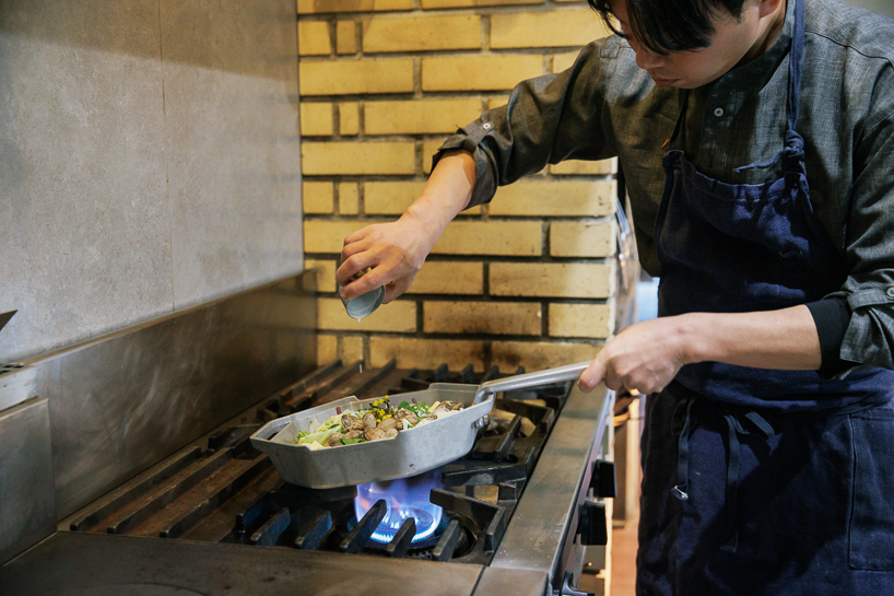 เชฟกำลังปรุงอาหารด้วยกระทะแปดเหลี่ยมบนเตาแก๊สในครัวร้านอาหาร