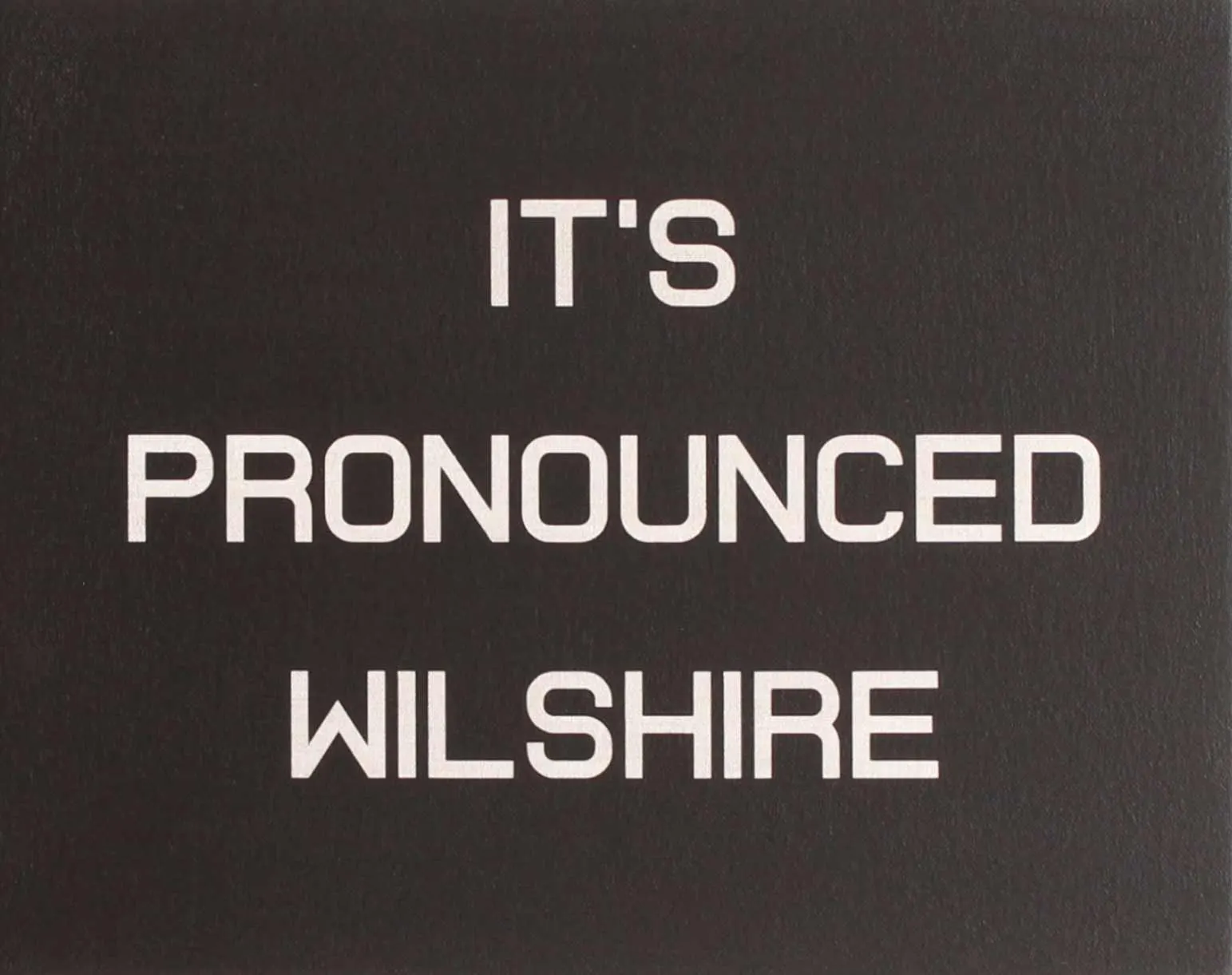 ภาพวาดข้อความ ITS PRONOUNCED WILSHIRE ตัวอักษรสีขาวเรียบบนพื้นเทาเข้ม