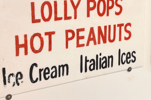 ป้ายร้านเขียนมือคำว่า LOLLY POPS HOT PEANUTS สีแดงและดำ
