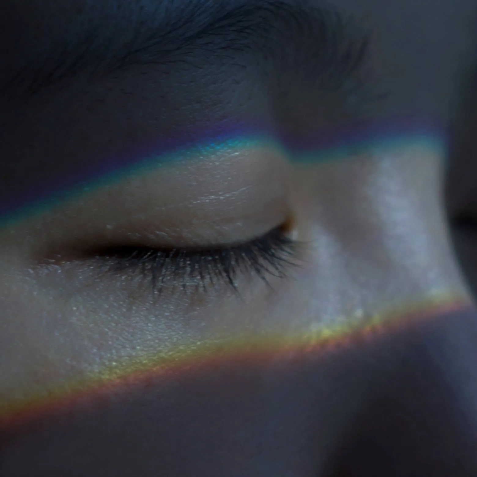 ภาพระยะใกล้ของดวงตาที่หลับอยู่ มีแถบสีรุ้งพาดผ่านคิ้วและแก้ม