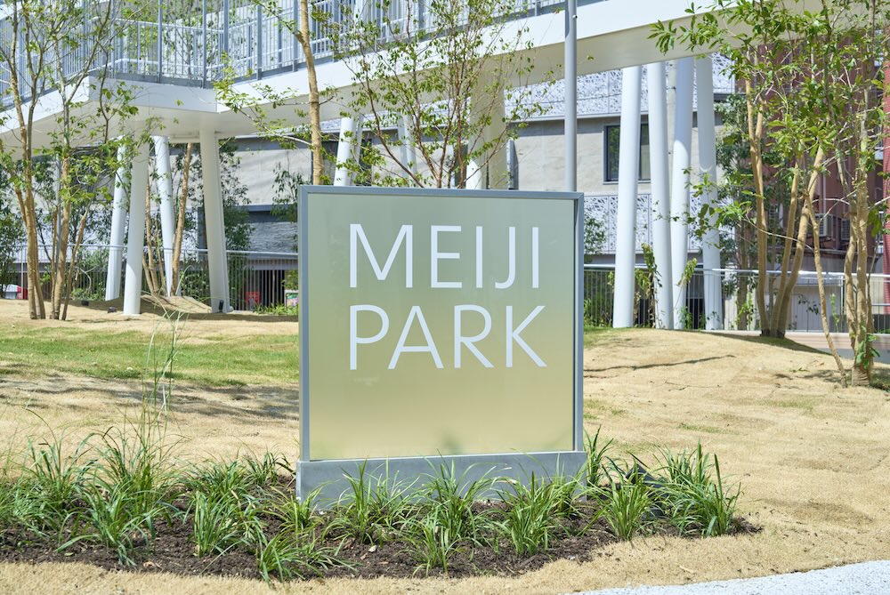 ป้ายชื่อ MEIJI PARK ตั้งอยู่บนสนามหญ้าใต้ทางเดินลอยของสวน