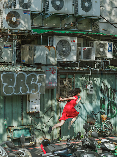หญิงชุดแดงลอยตัวหน้ากำแพงเครื่องปรับอากาศและกราฟฟิตี ผลงาน Today's Levitation ของ Natsumi Hayashi