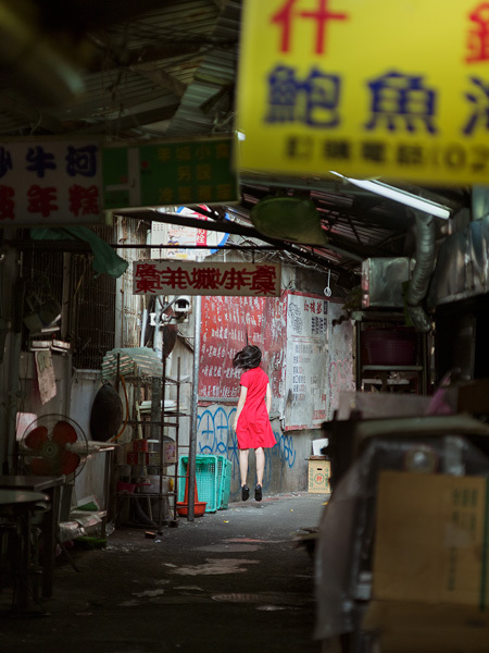 หญิงชุดแดงลอยตัวในตรอกตลาดที่มีป้ายภาษาจีน โดย Natsumi Hayashi