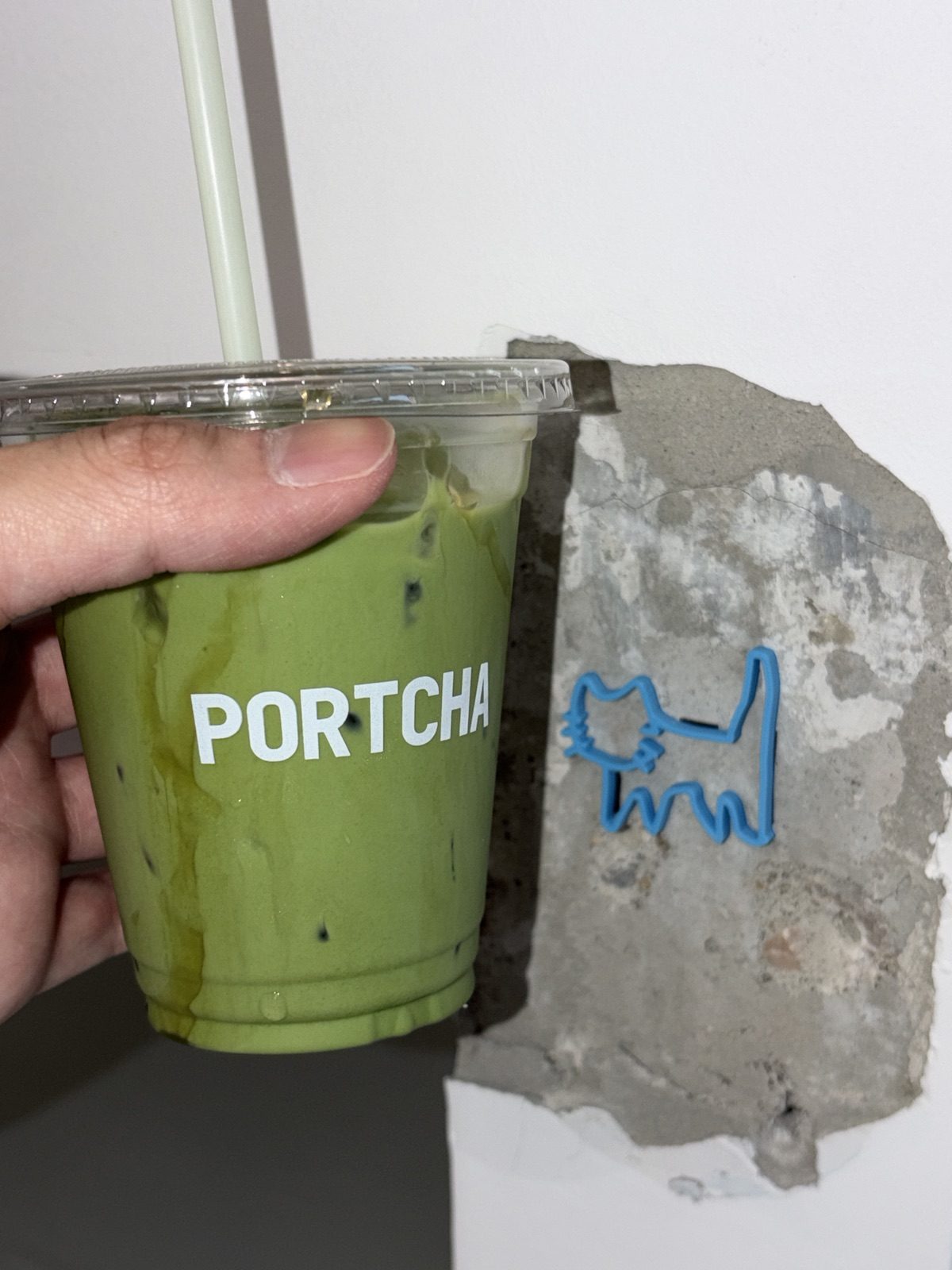 แก้วมัทฉะเย็น Portcha กับโลโก้แมวสีน้ำเงินบนผนัง